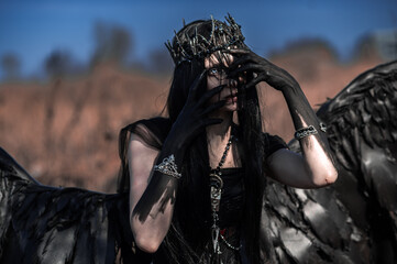 Naklejka premium Goddess of death with black wings on a dried field