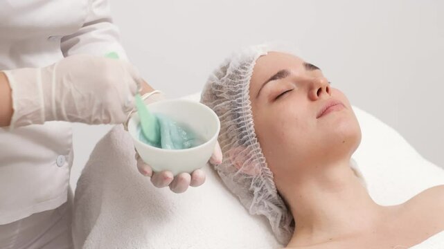 A young woman receives a revitalizing alginate face mask from a skilled cosmetologist in a sleek, modern beauty clinic. Perfect for promoting premium skincare treatments in your ads.