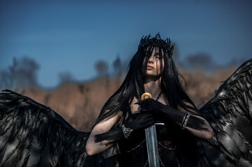 Obraz premium Goddess of death with black wings on a dried field