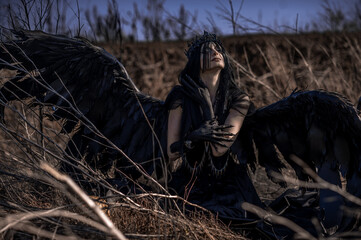 Obraz premium Goddess of death with black wings on a dried field