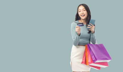 Young asian lady using mobile phone holding credit card carry shopping bags isolated over pastel green background and copy space Smiling young girl purchasing online through phone using credit card