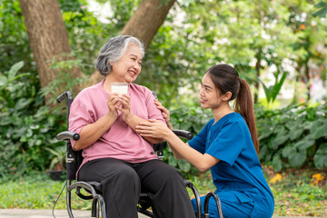Elderly woman in a wheelchair holding a cup of milk young healthcare worker stands assisting take care providing drink interaction reflects attentive caregiving, support is healthy treatment concept.