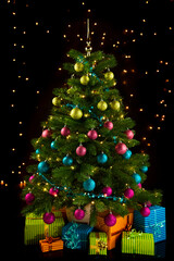 Illuminated Christmas tree with gift boxes, shining lights in background 