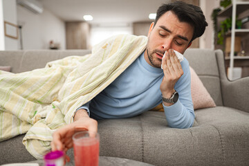 Sick man having a runny nose while lying on a sofa covered with blanket