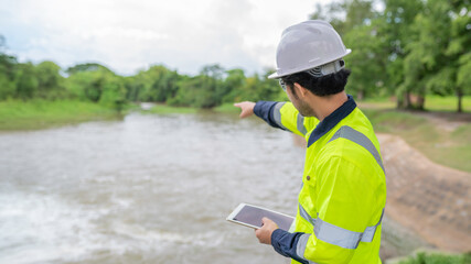 A engineering doing his checking routine. He is wearing hard hat and engineer uniform.Standing by the rail by the dam.Monitor water levels from the heavy rain that has been falling for several days.