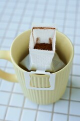 yellow cup freshly brewed coffee with convenient drip filter on kitchen table. prepare freshly brewed coffee at home. Space place for text. concept of making hot drink. bag of drip coffee beans.