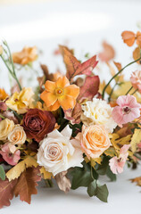 Fototapeta premium Bouquet of autumn leaves and light orange anemones, roses and ranunculus in a vintage vase.