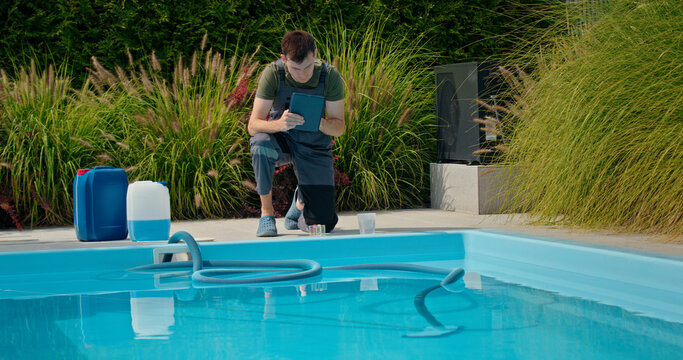Pool technician using a tablet by the pool, surrounded by chemical containers and greenery, focused on water quality. - Powered by Adobe