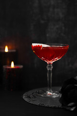 Vampire's Kiss Cocktail. Dracula's Blood Cocktail or Mocktail. Dark background, candle. Drink for Halloween with plastic vampire teeth as a garnish. Halloween festive food and beverages. Spooky season