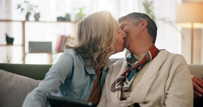 Mature, lesbian couple and tablet with kiss in home on sofa with social media scroll, watching video and relax. Lgbtq, people and romance with commitment, loyalty and trust in relationship on couch