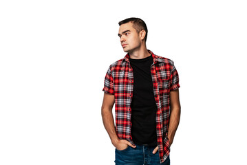 Fototapeta premium Young man in plaid shirt poses confidently against plain backdrop. A young man stands with his hands in his pockets, wearing a plaid shirt over a black t-shirt