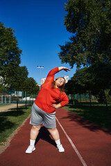 A joyful plus size woman stretches while exercising outdoors.