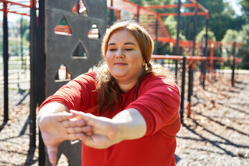 A plus size woman stretches gracefully in the park, embracing active living.