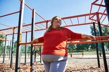 A beautiful plus size woman exercises joyfully in a sunny park setting.