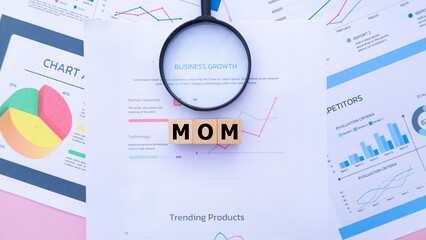 Three wooden cubes with the word MOM on graph sheets, abbreviation for Month Over Month. Business...