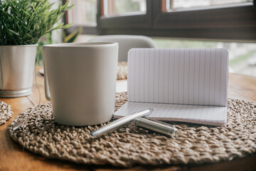 Notebook with pen and cup of coffee on wicker background.