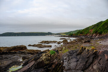 the South West Coast path along the Rame Peninsula in Mount Edgcumbe Country Park Cornwall England on a misty summer day with Kingsand and Cawsand in the distance