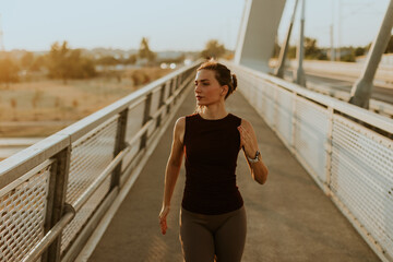 Determined runner jogs along a sunlit bridge during the golden hour, blending fitness and serenity in an urban landscape