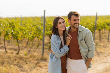 Couple strolls hand in hand along a sunlit path amidst lush vineyards during a warm afternoon