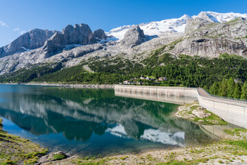 Fedaia lake and dam, water reflection, Marmolada massif group background with glacier. Dolomites mountain pass