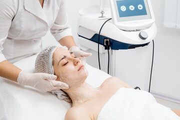 A skilled cosmetologist cleanses a young woman's face with specialized products in a modern beauty...