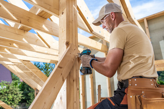 Skilled Carpenter at Work Constructing a Wooden Roof Frame in a Residential Home During Daylight