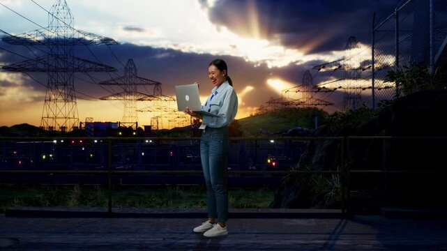 Full Body Side View Of An Asian Female Professional Worker Standing With Her Laptop Near High Voltage Tower, Industrial Facility, She Raises Her Fist Up With Screaming Goal After Typed On The Laptop