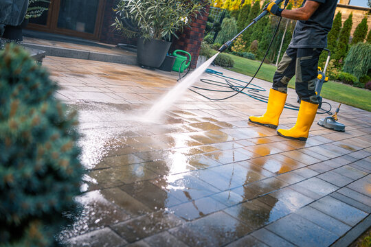 Man Cleaning Patio With Pressure Washer on a Sunny Day in a Well-Maintained Garden