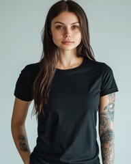 Obraz premium Young woman with sleeve tattoo in black T-shirt against neutral background offering design space