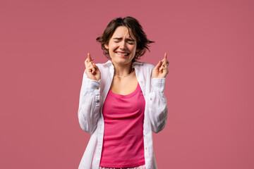 Stylish woman praying with crossed fingers, pink background.Lady begs someone