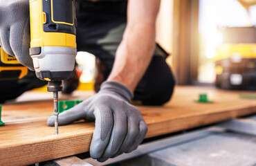 A Skilled Worker Uses a Power Drill on Wooden Planks During a Construction Project in Daylight