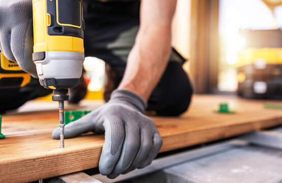 A Skilled Worker Uses a Power Drill on Wooden Planks During a Construction Project in Daylight