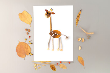 Delightful autumn nature craft for kids, featuring a giraffe made from a leaf. Body and neck crafted from leaf, smaller leaf forms head, yellow leaves as ears, twigs as antennae.,
