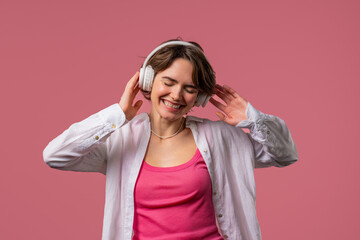 Young woman listening streaming music, enjoying dance with headphones on pink