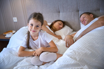 Obraz premium Girl sits near her parents on a large bed