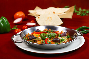 Spicy Shakshuka or Ojja merguez include poached egg, eggplant, capsicum, tomato, red and green chilli pepper served in pan dish isolated on red background side view of arabic food