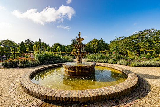 Inner gardens of Arcen Castle with an old baroque fountain with round pond, lush trees and a blue sky in background, sunny spring day in Limburg, Netherlands