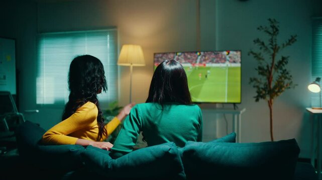 Two women sitting on a sofa are enjoying a football match on tv. They are discussing the game, sharing their excitement and passion for the sport
