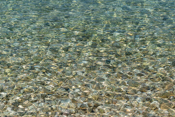 Rippling sea water surface, clear shallow water and stones at bottom