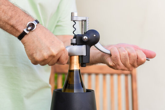 Close-up of man opening a wine bottle with a modern corkscrew