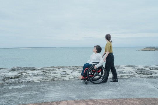 車椅子に乗った日本人女性が友人の女性と夏の沖縄を旅を楽しんでいる