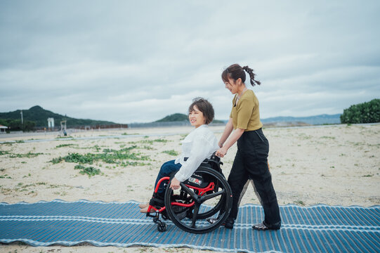 車椅子に乗った日本人女性が友人の女性と夏の沖縄を旅を楽しんでいる