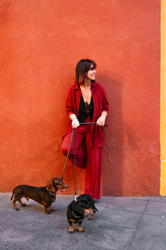 Young woman in red with two dachshund dogs on a sidewalk