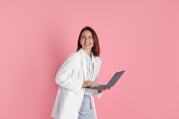 Beautiful woman in stylish white jacket with laptop on pink background