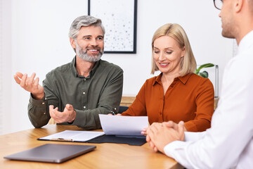 Pension plan. Couple consulting with insurance agent at table indoors