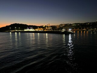 Beautiful sunset over the sea in Gozo seashore, Malta with the view on seashore with early city night lights. View from the boat