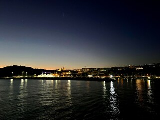 Obraz premium Beautiful sunset over the sea in Gozo seashore, Malta with the view on seashore with early city night lights. View from the boat