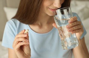 Woman with glass of water taking pill at home, closeup