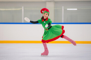 little girl figure skater dressed as a Christmas elf skates on the ice of an indoor arena.