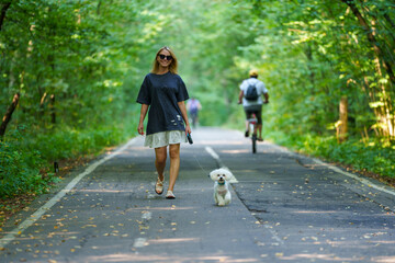 Fototapeta premium Girl walking the dog in the park forest. Rest concept. Woman walking with a dog on a leash during a good day